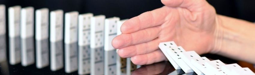 Clienti migliori: mano di uomo che blocca la caduta delle tessere del domino poggiate su un tavolo