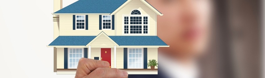 promuovere impresa edile: uomo sfocato sullo sfondo che con il braccio teso mostra un modellino di una casa