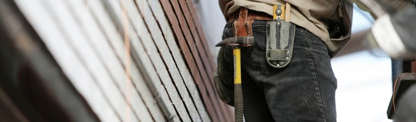 vendere più materiali edili: lavoratore con cintura da lavoro con martello e taglierino che sta lavorando in un cantiere